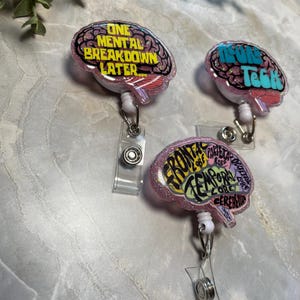 Puede incluir: Tres portatarjetas rosas con forma de cerebro con detalles brillantes. Cada uno presenta un dise&ntilde;o diferente con texto: "ONE MENTAL BREAKDOWN LATER", "NEURON TECH" y "FRONTAL LOBE, PARIETAL LOBE, TEMPORAL LOBE, CEREBELLUM".