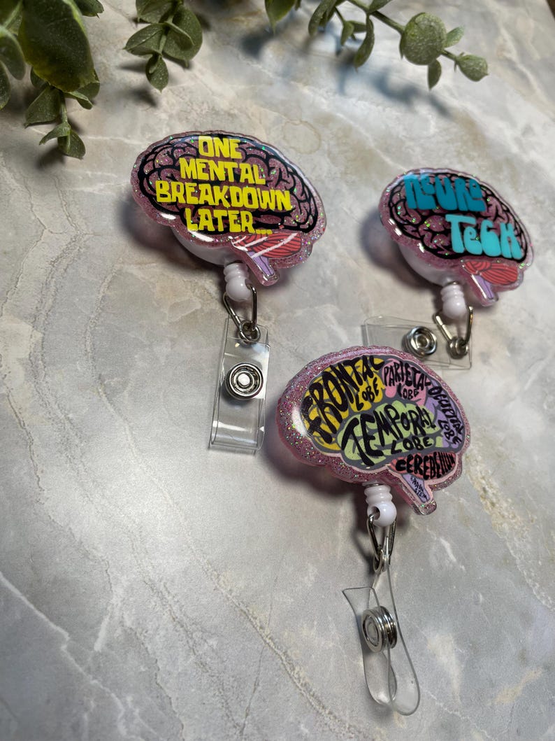 Puede incluir: Tres portatarjetas rosas con forma de cerebro con detalles brillantes. Cada uno presenta un dise&ntilde;o diferente con texto: "ONE MENTAL BREAKDOWN LATER", "NEURON TECH" y "FRONTAL LOBE, PARIETAL LOBE, TEMPORAL LOBE, CEREBELLUM".