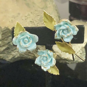 May include: A set of three blue and gold rose brooches with a distressed finish. The roses are made of metal and have a vintage look.