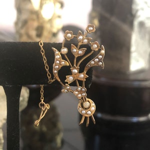 May include: A gold floral brooch with a delicate design featuring a cluster of pearl-like stones. The brooch has a chain attached to the back.
