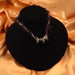May include: A black velvet necklace display with a silver skull necklace. The necklace is made of braided black and white yarn with silver skull beads.