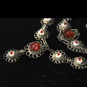 May include: A silver necklace with red and white glass beads. The necklace is made of delicate wirework and has a floral design.