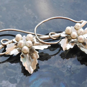 May include: A pair of silver earrings with a leaf design and pearl accents.