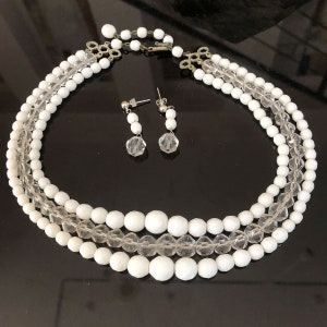 Puede incluir: Un collar de tres hileras de cuentas blancas con cuentas de cristal transparente. El collar se combina con pendientes de cristal a juego.