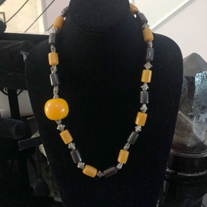 May include: A necklace made of yellow and brown beads with silver accents. The necklace features a large, round yellow bead in the center.