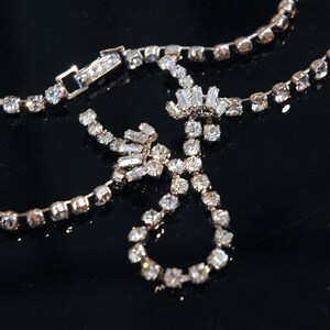 May include: A silver necklace with a delicate chain and a large, sparkling rhinestone pendant. The pendant is made up of several smaller rhinestones arranged in a floral pattern.