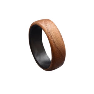 K&ouml;nnte beinhalten: Ein Holzring mit dunklem Innenraum. Der Ring besteht aus hellbraunem Holz mit sichtbarer Maserung. Der Innenraum ist dunkel, m&ouml;glicherweise schwarz. Der Ring hat ein schlichtes Banddesign.