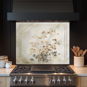 May include: A floral art piece with a gold frame is mounted above a stainless steel gas range. The artwork features a bouquet of beige and yellow flowers against a marble-like background. The kitchen design has a modern aesthetic.