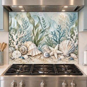 Op de afbeelding: Een keukenachterwand met een aquarelillustratie van een onderwaterscène met diverse schelpen, een witte zeester, koraal en zeewier in blauwe, groene en beige tinten, geplaatst achter een roestvrijstalen gasfornuis.