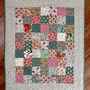 May include: A patchwork quilt with a floral pattern in shades of red, pink, green, and cream. The quilt is made of small squares and has a floral border. The quilt is likely handmade and suitable for a bed or wall hanging.