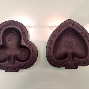 May include: Two dark brown decorative dishes, one shaped like a club and the other a spade. Each dish has a detailed relief design of figures and a laurel leaf border. The club dish has three sections, while the spade dish has one.