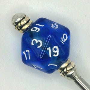May include: A blue, twenty-sided die with white numbers, mounted on a silver-colored metal stick. The die is a deep blue color with a marbled effect. The top and bottom of the die are capped with silver-colored metal. The die is a gaming accessory.