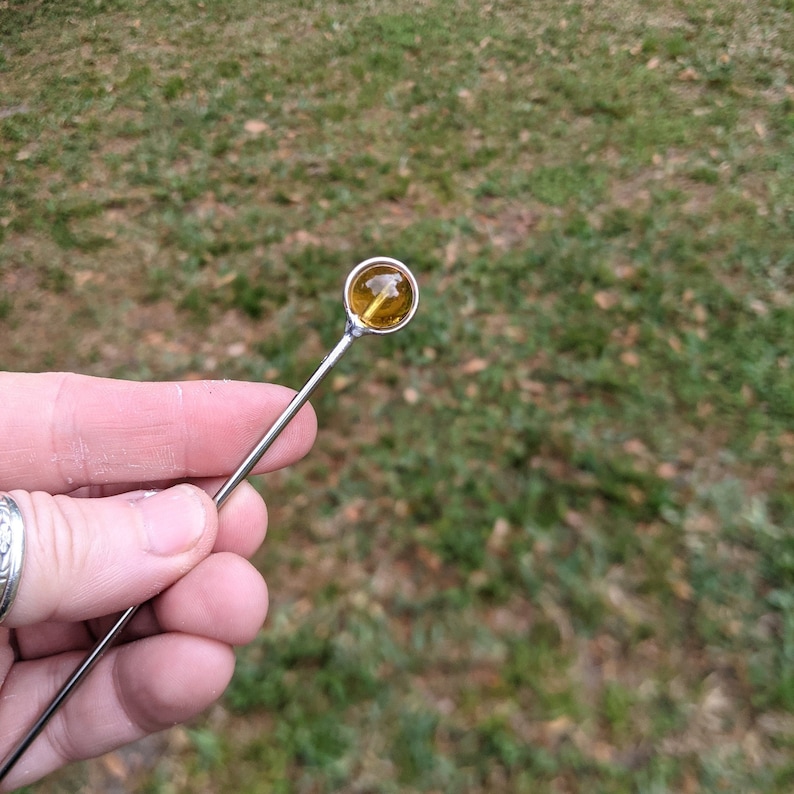 May include: A silver stirring rod with a round, amber glass bead at the top.