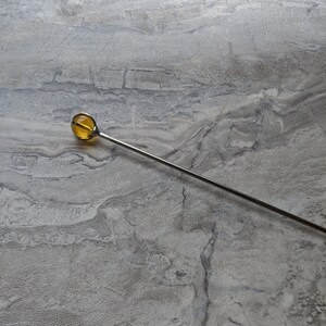 May include: A silver metal stirring rod with a round, amber-colored glass tip.