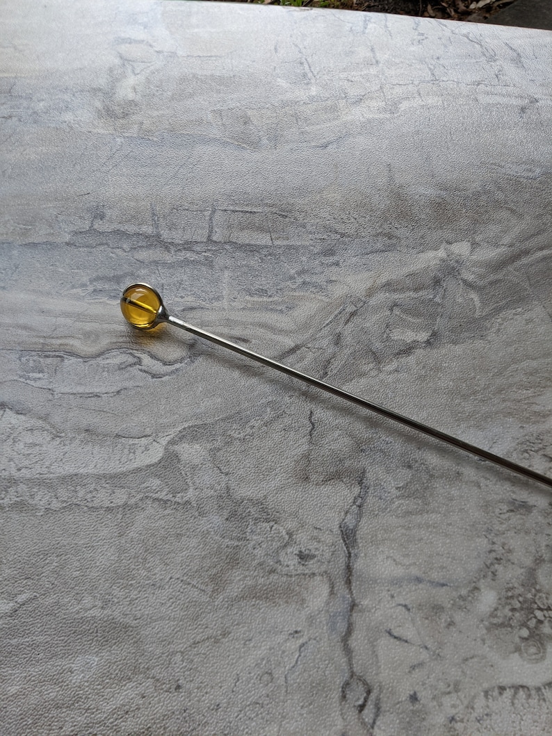 May include: A silver metal stirring rod with a round, amber-colored glass tip.
