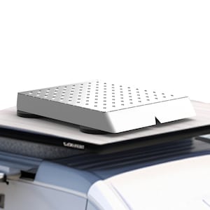 Puede incluir: Un portaequipajes de techo rectangular de metal blanco con una superficie texturizada. El portaequipajes está montado en un coche blanco.