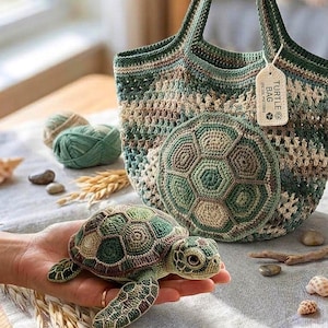 May include: A handmade crochet turtle bag with a matching turtle applique. The bag is green, brown, and beige. A small crochet turtle is held in a hand. The tag on the bag reads "Turtle Bag (Crochet Pattern)".
