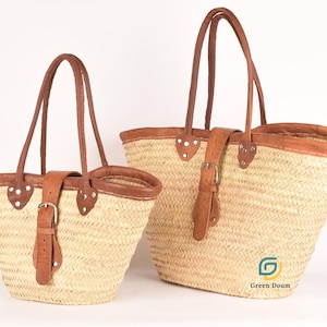 Peut inclure: Deux sacs fourre-tout en paille tressée avec garnitures, poignées et fermetures à boucle en cuir marron. Les sacs sont de tailles différentes, le plus grand étant à droite. Les sacs sont de couleur marron clair naturel et le cuir est marron foncé.