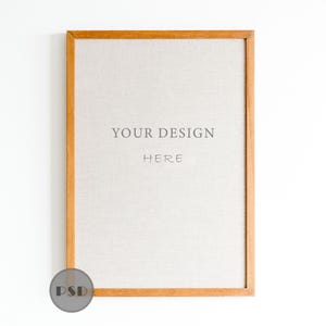 May include: A rectangular wooden picture frame with a light-colored linen-like insert. The text "YOUR DESIGN HERE" is centered on the insert. The frame is a warm, light brown color, and the background is white.