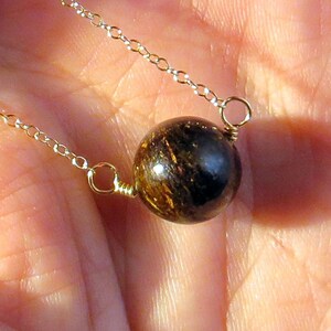 May include: A gold chain necklace with a single round brown and gold gemstone pendant.