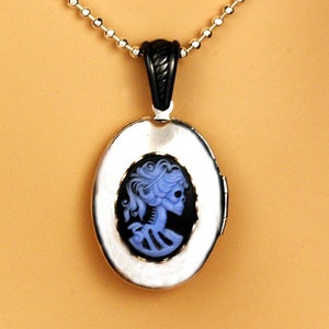 May include: A silver locket necklace with a black chain. The locket features a cameo of a blue skeletal woman with black hair.