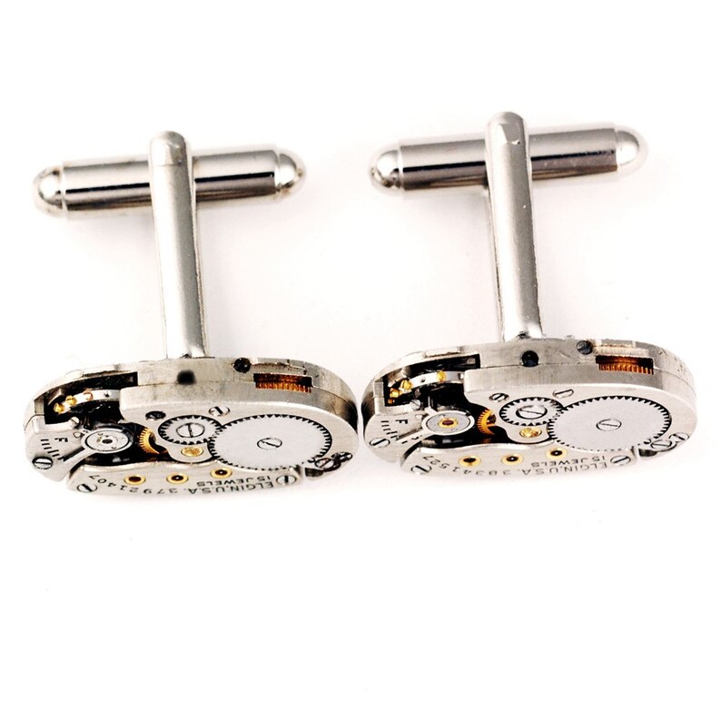 Pode incluir: Um par de bot&otilde;es de punho de prata com um design de movimento de rel&oacute;gio em tom dourado. Os bot&otilde;es de punho apresentam o texto "ELGIN USA 15 JEWELS" na face.