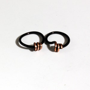 May include: Two black hoop earrings with a copper accent. The copper accent is a coil of wire.