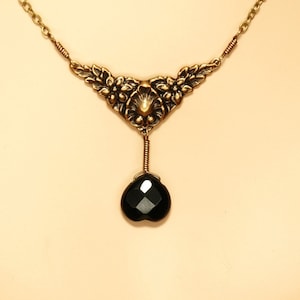May include: A gold necklace with a floral design and a black gemstone pendant.