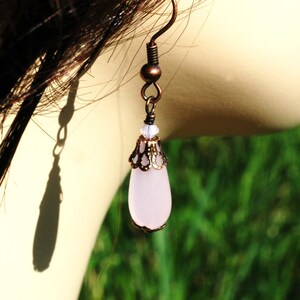 May include: A pair of dangle earrings with a pink teardrop-shaped glass bead and a copper filigree design.