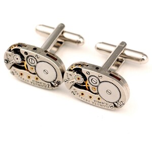 Pode incluir: Um par de bot&otilde;es de punho de prata com um design de movimento de rel&oacute;gio vintage. Os bot&otilde;es de punho apresentam o texto "ELGIN USA 15 JEWELS 36327" e "ELGIN USA 15 JEWELS 37320Y".