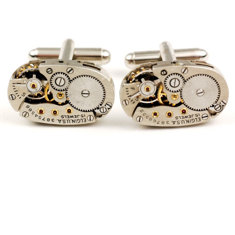 Pode incluir: Um par de bot&otilde;es de punho de prata com um design de movimento de rel&oacute;gio vintage. Os bot&otilde;es de punho apresentam o texto "ELGIN U.S.A. 3674588 15 JEWELS" e "ELGIN U.S.A. 3766924 15 JEWELS".