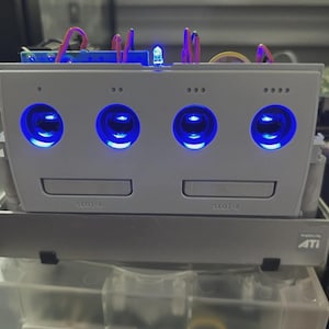 May include: A modified, light gray video game console with four glowing blue lights and the text "SLOT-A" and "SLOT-B". The console is stacked on top of another component with the "ATI" logo.