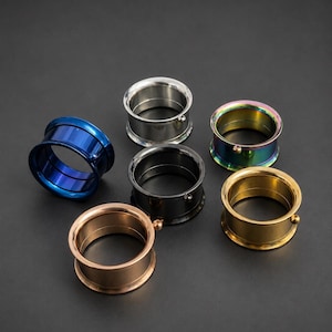Op de afbeelding: Een verzameling van zes ronde oortunnels in diverse metallic afwerkingen, waaronder zilver, goud, roségoud, zwart, blauw en iriserende regenboogkleuren. Elke tunnel heeft een glad cilindrisch lichaam met een klein kraaldetail op de buitenrand.