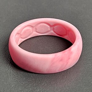 May include: A pink silicone ring with a marbled effect. The inside of the ring features a series of oval-shaped cutouts. The ring is a solid, rounded band, suitable for everyday wear.