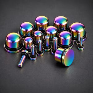 May include: A collection of iridescent rainbow-coloured ear plugs and tunnels in various sizes. Each piece features a smooth, metallic finish with a spectrum of blue, green, purple, and yellow hues, and includes a black rubber O-ring for secure placement.