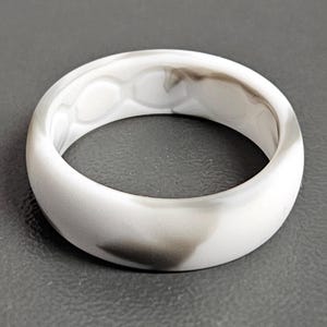 May include: A white and gray marbled silicone ring. The ring has a smooth, rounded design with a marbled pattern of white and gray swirls. The ring is a simple band, suitable for everyday wear.