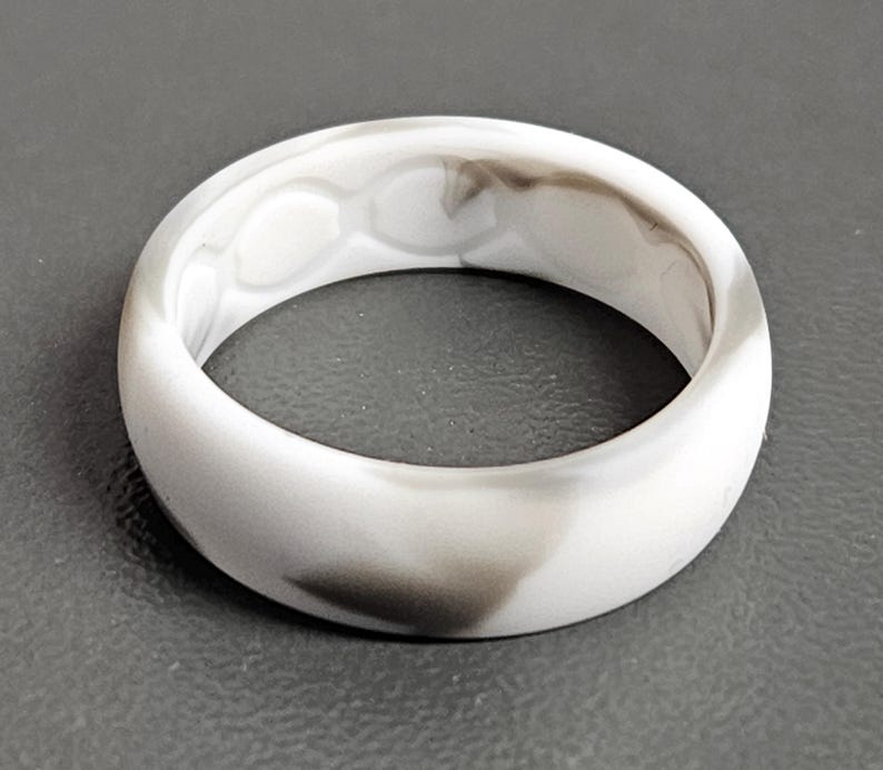 May include: A white and gray marbled silicone ring. The ring has a smooth, rounded design with a marbled pattern of white and gray swirls. The ring is a simple band, suitable for everyday wear.