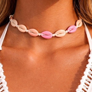 Peut inclure: Un collier ras du cou composé de coquillages roses et pêche alternés, enfilés sur un cordon blanc. Ce bijou délicat est parfait pour ajouter une touche de charme côtier à n'importe quelle tenue.