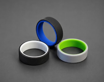 May include: Three silicone rings arranged in a cluster. One ring is black with a white interior, one is black with a blue interior, and one is light gray with a bright green interior. Each band features a smooth, matte finish and a flat profile.