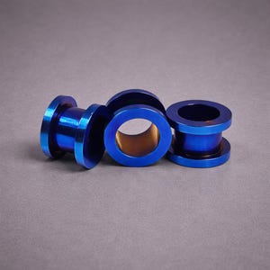 May include: Four blue tunnel ear gauges are shown against a grey backdrop. The gauges have a cylindrical shape with a flared edge on each side. The interior of the gauges has a gold colour. The gauges are made of metal.