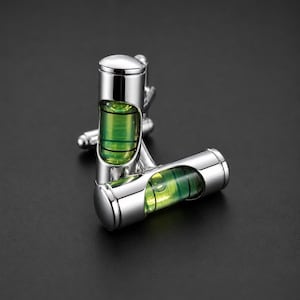 May include: A pair of silver cufflinks with a level design. Each cufflink features a cylindrical body with a green and yellow bubble level. The cufflinks are set against a dark background.