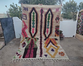 May include: A colorful Moroccan rug with a geometric pattern in shades of pink, yellow, green, and black. The rug has a white background and is made of wool.
