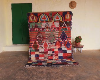 May include: A colorful Moroccan rug with geometric patterns in shades of red, blue, green, and white. The rug has a fringe border and is made of wool.