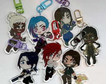 Könnte beinhalten: Satz mit neun bunten Anime-Charakter-Schlüsselanhängern. Jeder Schlüsselanhänger zeigt einen anderen Charakter mit einzigartigen Designs und Farben. Die Schlüsselanhänger sind aus klarem Acryl gefertigt und haben Metallringe zum Anbringen an Schlüsseln oder Taschen.