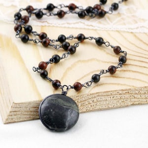 May include: A black and brown beaded necklace with a large, round, black and green stone pendant.