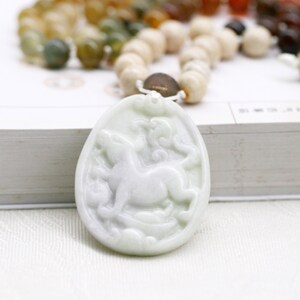May include: White jade pendant with a carved image of a horse. The pendant is attached to a beaded necklace with brown, white, and green beads.