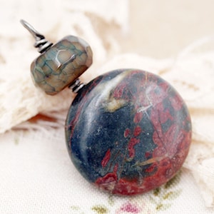 May include: A pendant necklace featuring a round, dark blue and red stone with white veins and a smaller, faceted, brown and green stone.