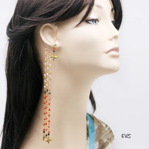 May include: An ear cuff with dangling strands of colorful beads. The ear cuff features gold-colored bee charms and a cascade of pink, red, and black beads. The design is attached to a copper-colored ear wire.