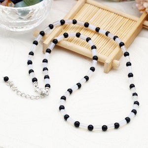 May include: A black and white beaded necklace with a silver clasp. The necklace is made of small, round beads.