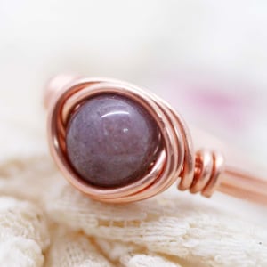 May include: A rose gold wire wrapped ring with a purple gemstone.